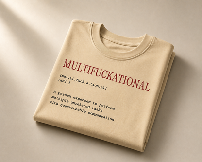 A folded beige T-shirt with a humorous dictionary-style definition printed on the front in red and black text, displayed on a neutral beige background with soft diagonal shadows.